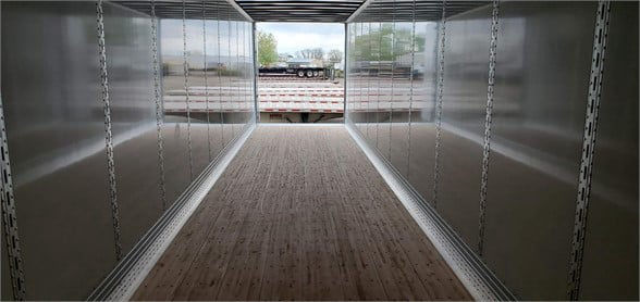 Interior view of a 2024 Vanguard VXP dry van trailer showing metal sidewalls, a wood grain floor, and an open rear showing exterior scenery.