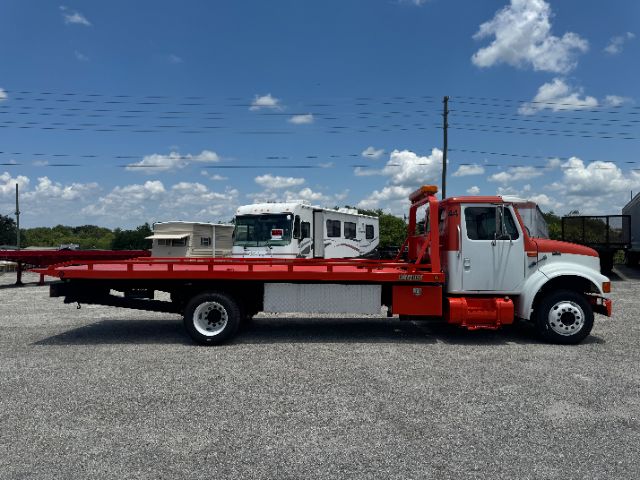 Truck cab with flatbed tow truck body, International 4700 DT 466E, red flatbed and white cab, side view.