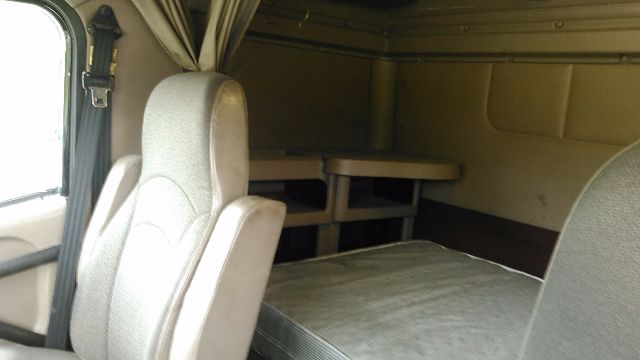 Truck cab interior with sleeper area and bed, two front seats, table and storage shelves visible.
