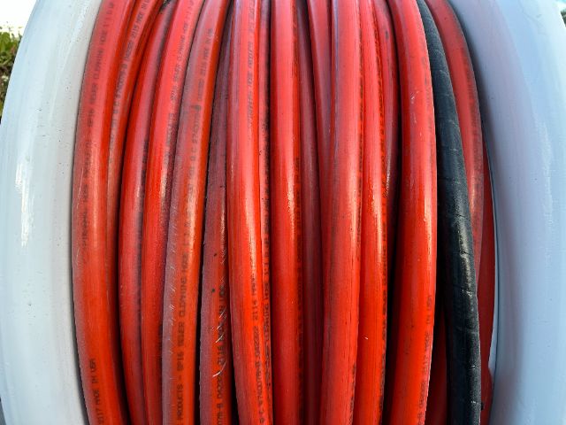Coiled red and black hydraulic hoses or cables mounted in a reel on a truck equipment, with visible text along the hoses.