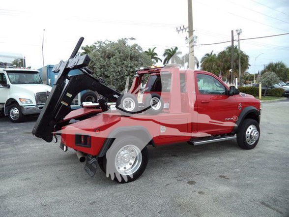 2021 Ram 4500 SLT tow truck with a tilt bed in a red color. Visible text on stickers includes VIN or stock numbers not legible. The vehicle is parked outdoors with other trucks nearby.