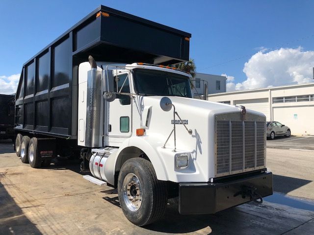 Kenworth T800 dump truck with a large black dump bed and white cab, parked outdoors.