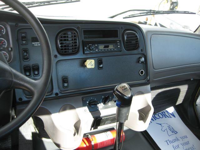 Cab interior of Freightliner M2106 with manual shifter, dashboard, steering wheel, and radio/display panel.