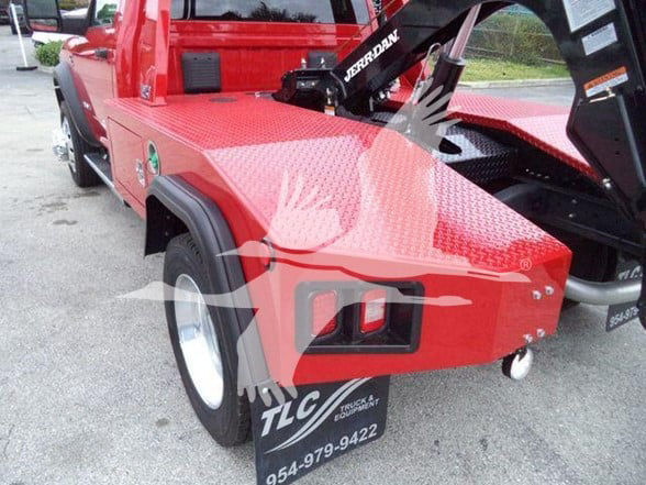 Red tow truck rear quarter with diamond plate toolbox, wheel, TLC Truck & Equipment license panel, and a small white tow hook. Visible text includes TLC Truck & Equipment, phone number 954-979-9422.