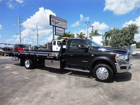 2024 Ram 5500 SLT tow truck with a flatbed, black cab, chrome wheels, and stock number J67261 visible on sign in lot.