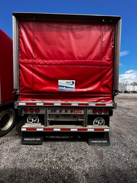Rear view of a red curtain-side trailer with a roll tarp, showing taillights, bumper, and mud flaps. Visible text includes 'RANDOLPH OHIO' on mud flaps, '50' wheel logos, and a small center plate with numbers.