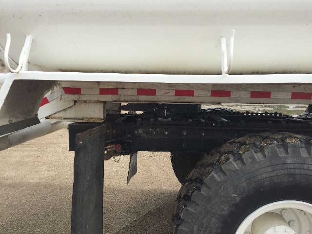 Truck undercarriage showing the rear wheel and frame with a white tanker behind, part of a military M923A1-style truck.