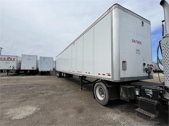 Rear and side view of a white 2018 Vanguard VXP trailer with red stock number 847908 and support jack, parked among other trailers.