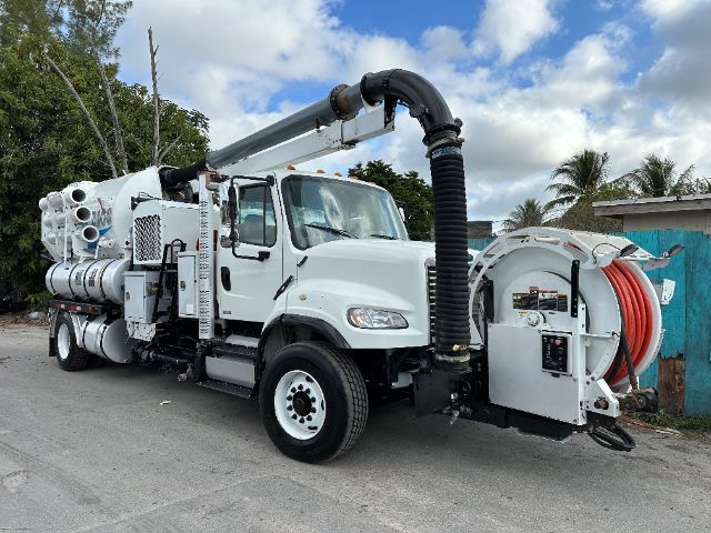 Freightliner M2 vacuum truck with long black hose reel and rear suction setup; white cab and equipment; several labels and control panels on side; large hose reel at back.