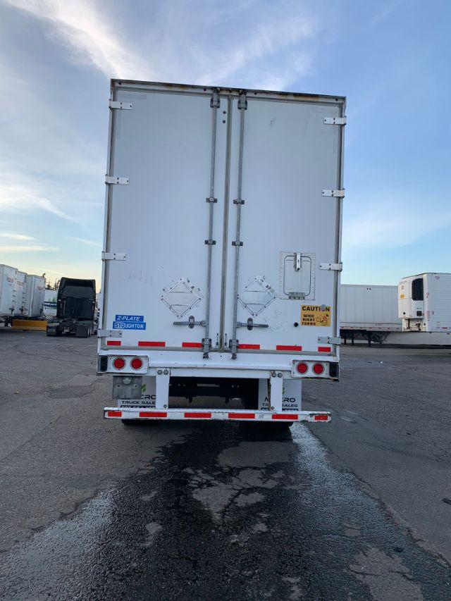 Rear view of a white 2017 Stoughton dry van trailer with double doors. Various stickers and reflective tape visible, including a blue '2-PLATE STOUGHTON' plate and a yellow caution label.