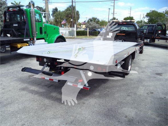 Flatbed tow truck trailer with ramp in rear, International CV pickup truck in background, stock area lot.
