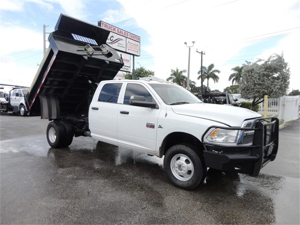 White 2012 Ram 3500 SLT dump truck with hydraulic bed raised, front grille guard, side mirrors, dual rear wheels, on wet pavement.