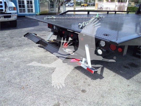 Tow truck flatbed rear showing hydraulic ramp and chain tie-downs with reflective lights.