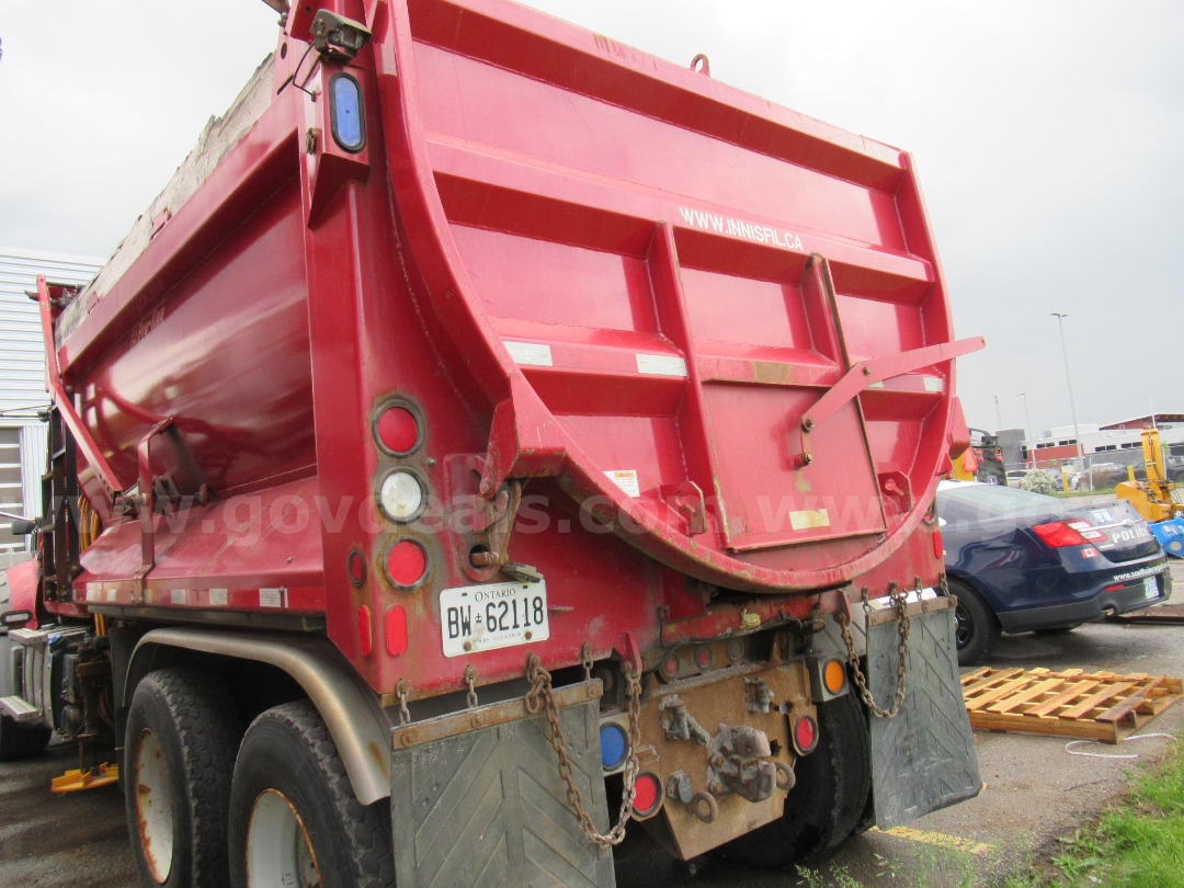 Rear view of a red 2014 Mack GU713 dump truck with Ontario license plate BW 62118 and chains on the mudflap area.