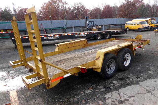 Trailer with dual-axle flatbed and ramp, yellow paint, wooden deck, tow hooks and ramps visible.