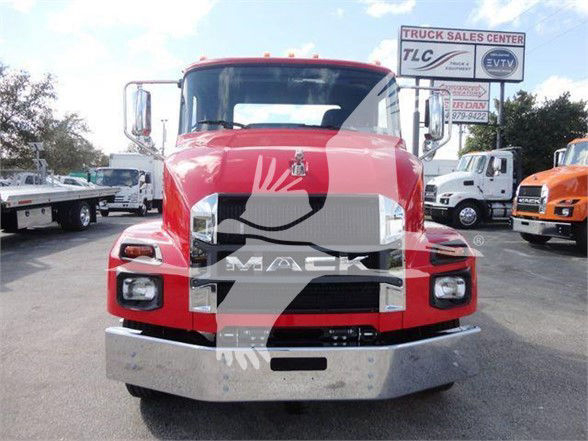 Mack MD6 truck front view in red with chrome grille and bumper; large windshield, side mirrors, and factory signs in background.