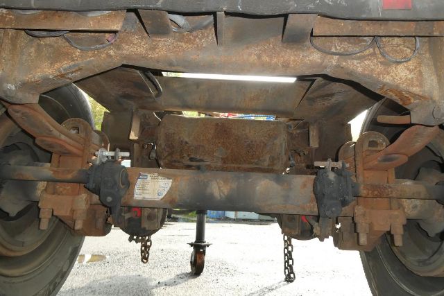 Underneath view of a used Dolly trailer with rusty undercarriage, showing rear axle, leaf springs, chain hooks, and label on the center crossbeam.