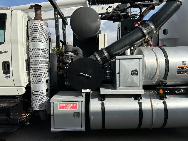 Truck side view with vacuum system components including large cylindrical silencer, silver fuel/air tanks, and metal boxes with labels.
