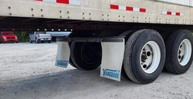 Trailer undercarriage showing three axles with tires and Vanguard mud flaps. Visible text includes 'VANGUARD' on mud flaps and trailer frame details.