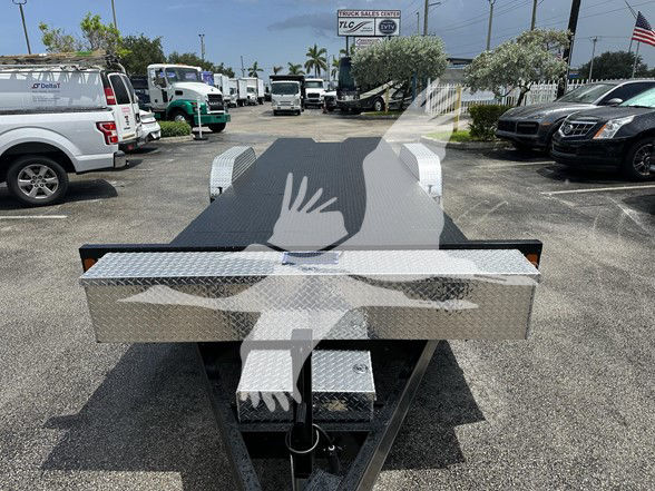 Flatbed trailer tongue area with diamond plate toolbox and hitch. Partial view shows two rectangular lighted fenders and a front toolbox mounted on a black frame.