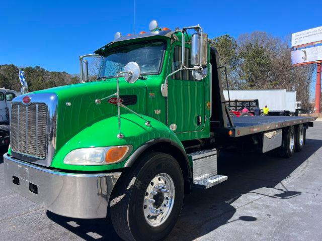 Green Peterbilt 348 rollback truck with flatbed, chrome front bumper, dual rear axles, and side steps.