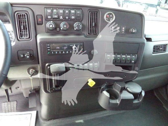 Interior of a 2025 International MV cab showing dashboard controls, vents, cup holders, and a yellow caution tag.
