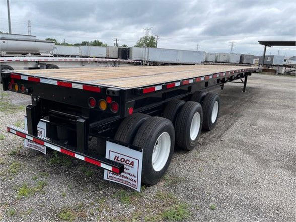 Flatbed trailer with three axles and wooden deck, Fontaine XCALIBUR extendable, rear with taillights, reflectors, and IL OCA mudflaps. Visible text: 'ILOC A' on mudflaps, stock numbers and labeling on plates.