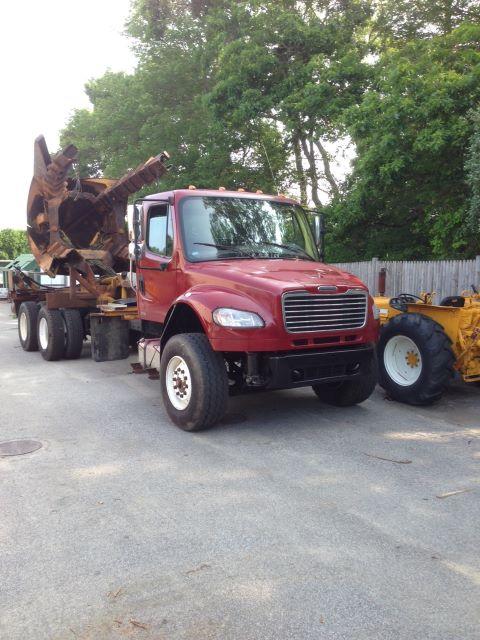 Truck in yard showing front-left view of a red 2008 Freightliner M2106 cab chassis with large front grille and dual rear wheels in background.