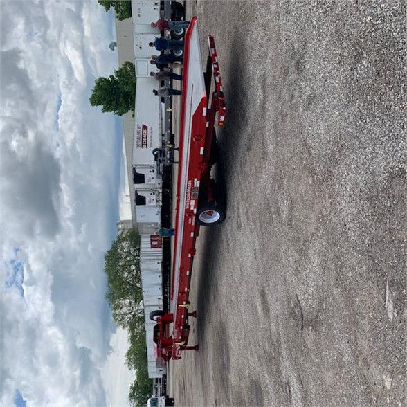 Red drop deck container delivery trailer with single axle in an outdoor lot, side view showing frame and deck.