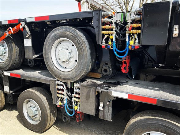 Truck trailer side showing dual axles, spare wheel, and hydraulic lines with colorful fittings on a trailer deck.