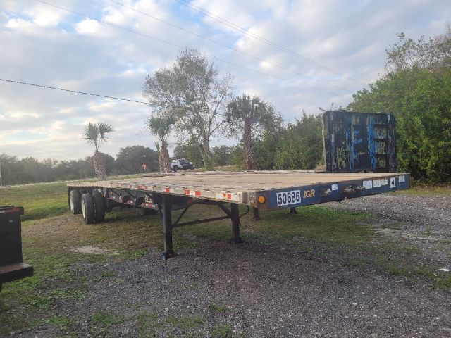 Flatbed trailer 48x102 with tandem axles, used Great Dane trailer, low ground clearance, tag number 50686 on front; blue container at rear and trees in background.