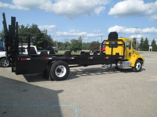 Kenworth flatbed truck with yellow cab and long black flatbed, side-view showing seating area and rear equipment.