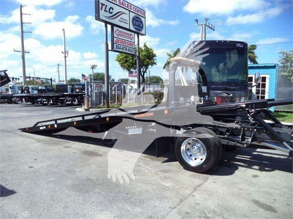 Ram 5500 tow truck flatbed in showroom lot with signboard in background, stock number J24798.