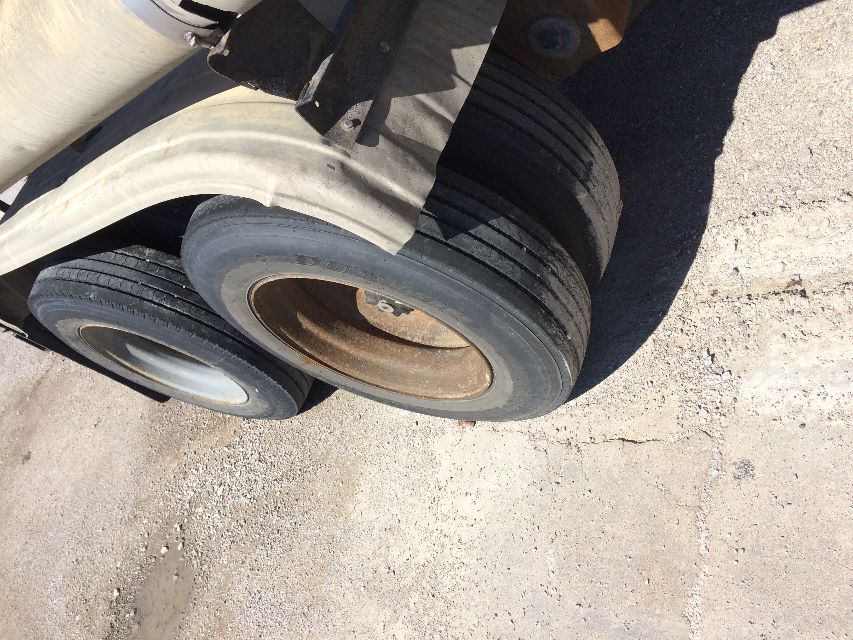 Wheel area of a Fruehauf pneumatic dry bulk trailer showing dual rear tires with rims, exposed suspension, and part of the beige/gray side wall.