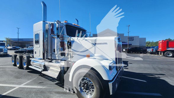 Kenworth W900L truck in a dealership lot, front-left angle, chrome exhaust stacks, white paint.