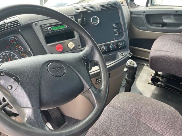 Dashboard and steering wheel inside a Freightliner Cascadia truck cab showing gear shifter and controls.