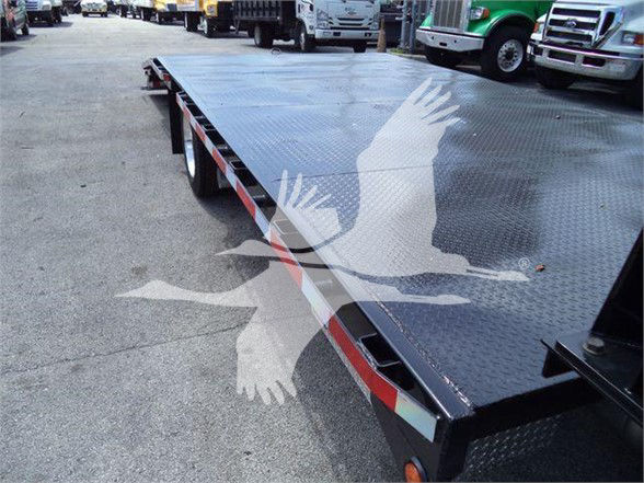 Flatbed tow truck trailer with diamond plate surface and red-and-white reflective striping, multiple trucks in background.