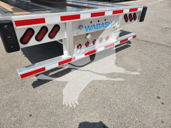 Wabash trailer rear bumper with red/white reflective tape and lights, branding 'WABASH' on white metal surface.
