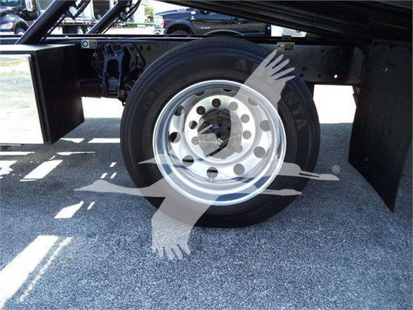 Front wheel and tire of a Peterbilt 337 truck chassis with metal hub and lug nuts visible; undercarriage and frame sections; reflective wheel well cover nearby.