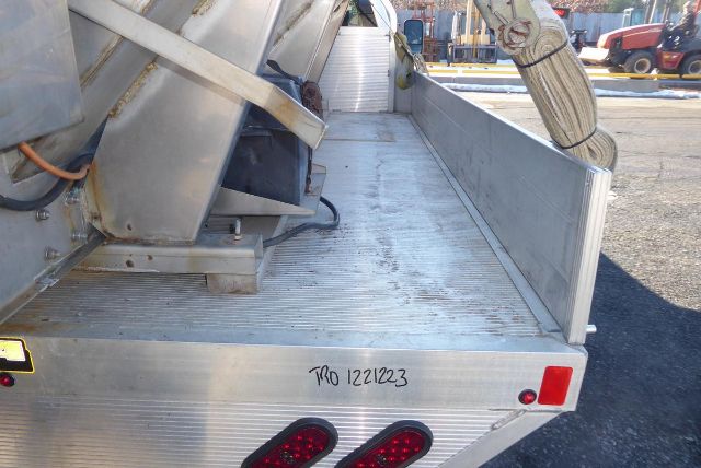Flatbed utility truck bed with metal ramp and storage, rear view showing tail lights and handwritten stock number 1221223 on the tailgate.