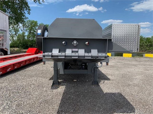 Image shows a 2024 drop deck container delivery trailer with tandem axles. Front view reveals a steel ramp/bed with latching brackets and a diamond-plate toolbox on the side.