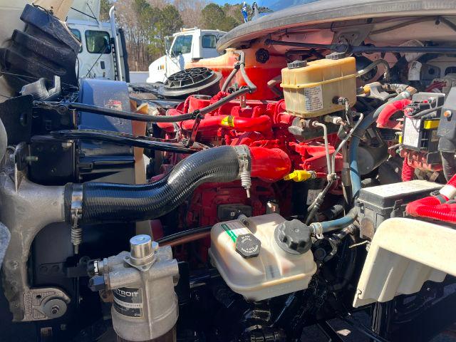 Truck engine bay of a 2018 Freightliner M2 106 dump truck showing red engine components, hoses, coolant reservoir, and various fluid reservoirs.