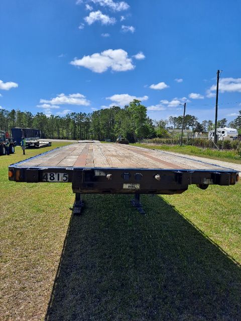 Flatbed trailer viewed from side with long wooden deck, Fontaine logo likely on front, clear sky and grassy area.