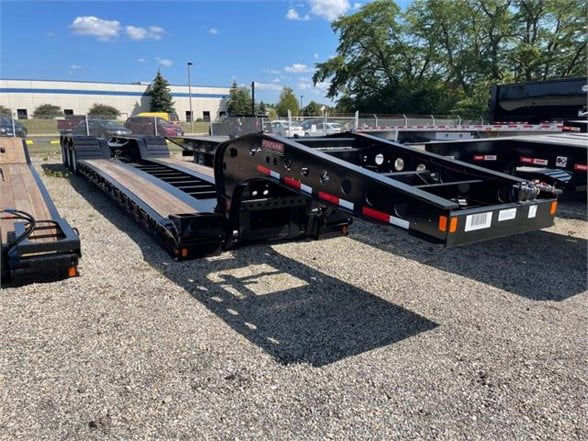 Lowboy trailer with long deck and black steel frame. Visible labels: Fontaine branding on side near hitch, warning labels and reflective tape on rear, multiple mounting points along deck.