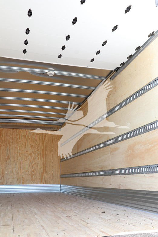 Interior of a new 2025 Hino L6 cab and chassis cargo truck box; wooden walls with metal E-track rails and a white oak floor, showing no engine components.