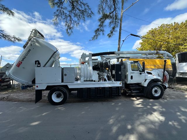 2009 International 7500 vacuum truck with a mounted vacuum system and concrete debris hose, side view under a partly cloudy sky.