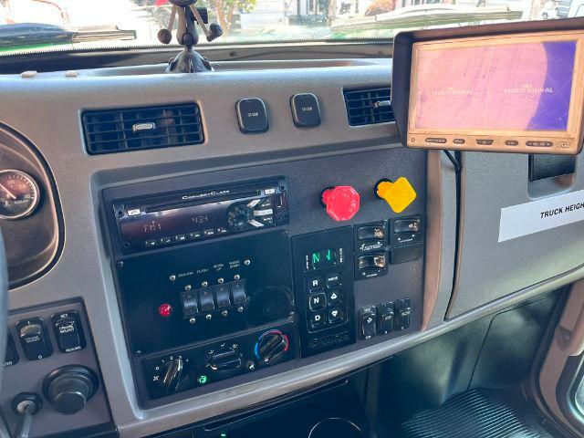 Dashboard of a 2015 Peterbilt 348 rollback truck showing instrument cluster, gear shifter panel, red and yellow controls, and a screen mounted to the right.