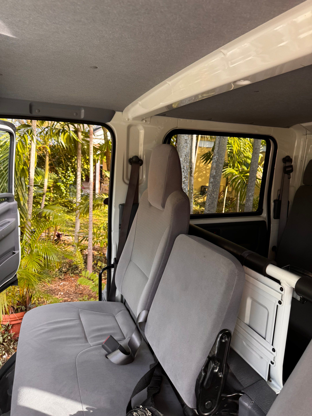 Isuzu NQR interior with front passenger seat and open door, showing grey cloth seats, seat belts, and cargo partition in a box truck cab.