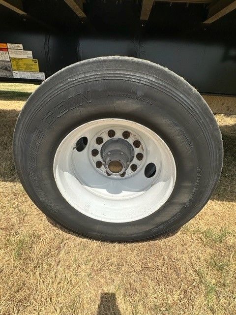 Trailer wheel/rim close-up showing tire labeled 'MR244' and white steel wheel on a flatbed trailer.