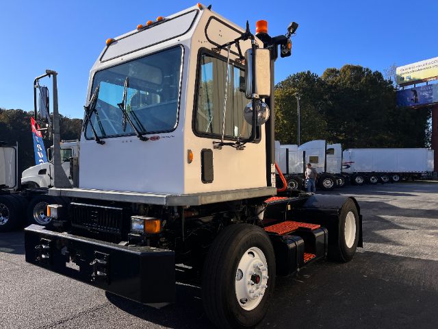 Vehicle chassis with cab only showing front view of a white truck cab, orange marker lights, and side mirrors in a yard.